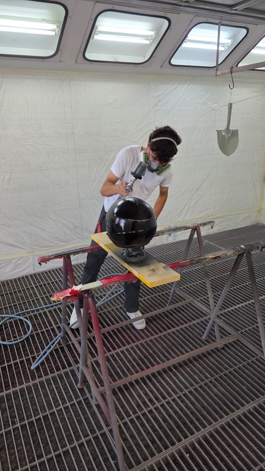 Cristian a spruzzo su un casco nero in cabina di verniciatura