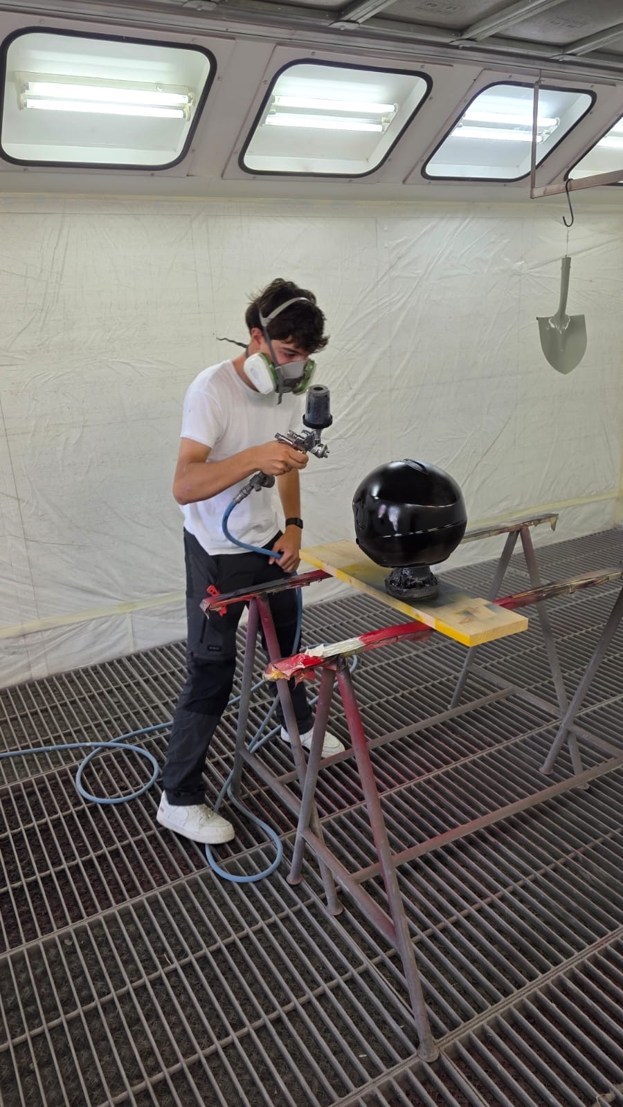 Cristian in piedi in cabina mentre vernicia il casco nero con la pistola