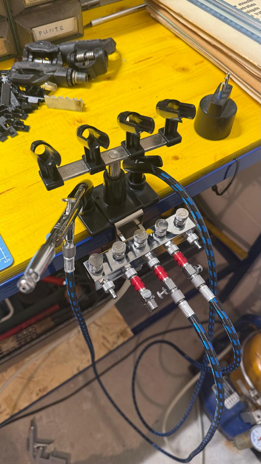 Postazione con collettore aria compressa, regolatori e supporto aerografi sul banco giallo